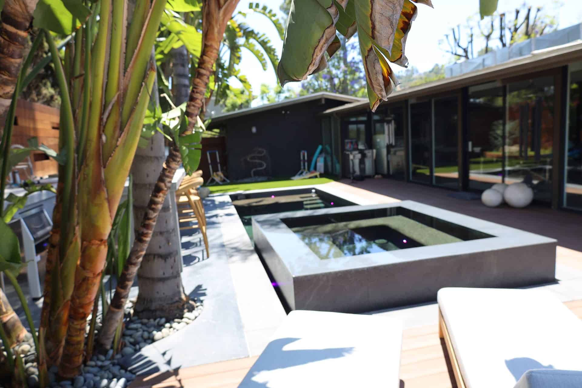 Dark-finish pool and raised spa beside a mid-century home, palm-shaded deck