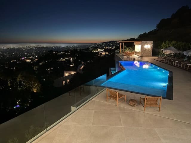 Vanishing-edge pool lit at dusk above the city lights, glass rail at the edge
