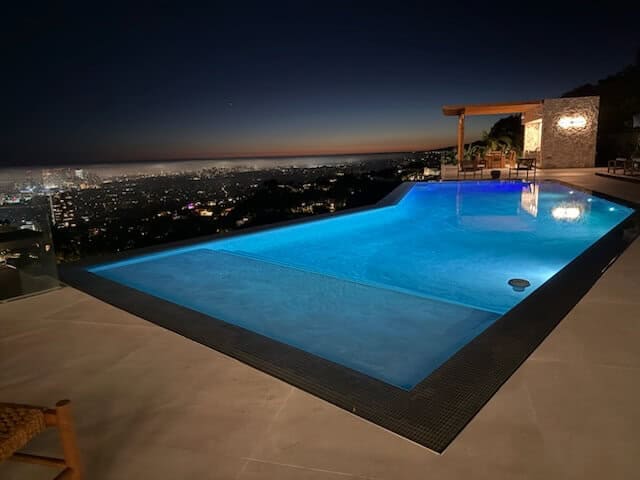 Pool lit blue at night on a hillside, city lights on the horizon