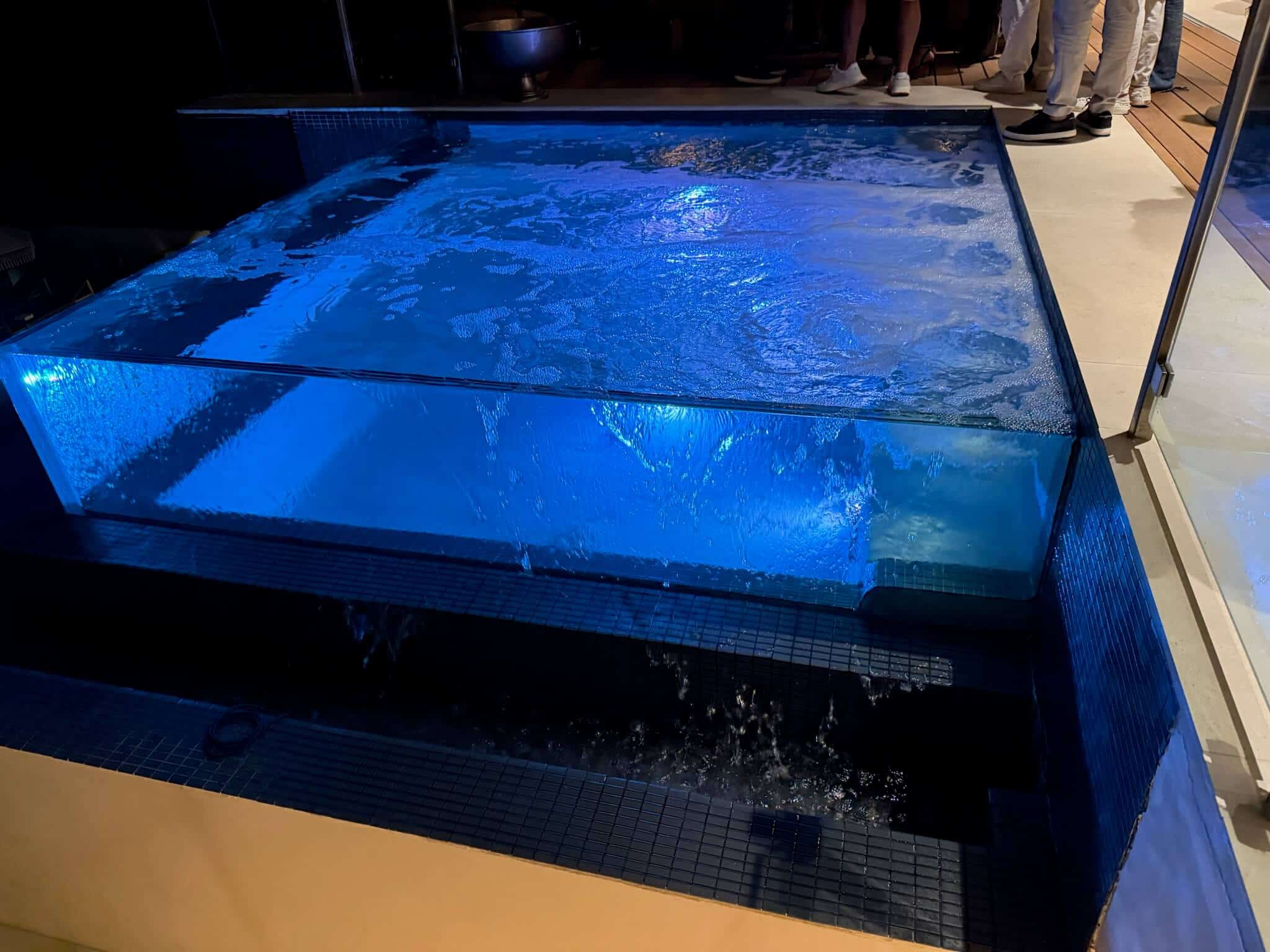 Glass-walled raised spa with a perimeter overflow spilling into the pool below